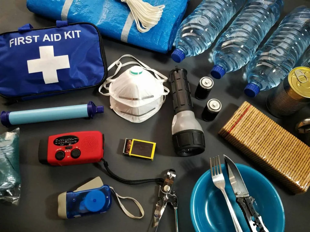 Hurricane preparedness kit with water, first aid supplies, flashlight, radio, batteries, and canned food.