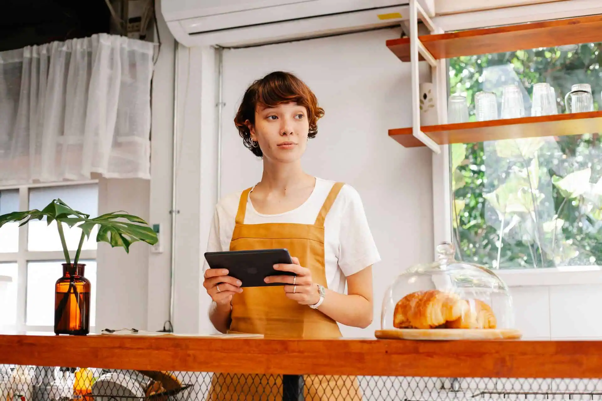 Small business café owner holding a tablet behind the counter while reviewing POS and payment security.