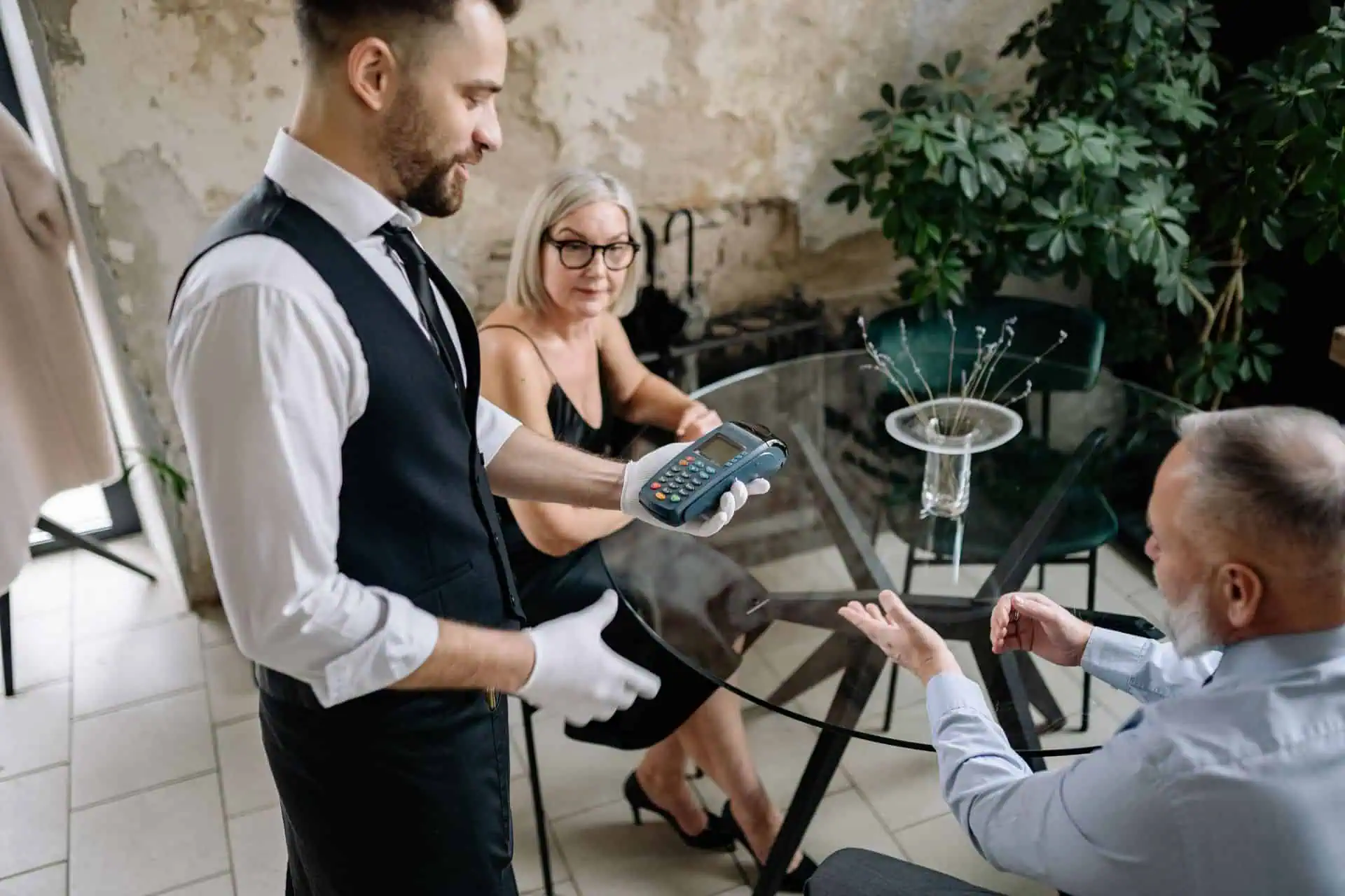 Older couple paying their restaurant bill with a waiter holding a card terminal.